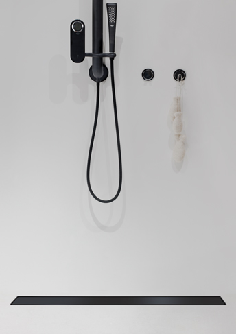 Elegantais ACO Showerdrain Black ar melnu dušas klausuli uz balto flīžu fona.