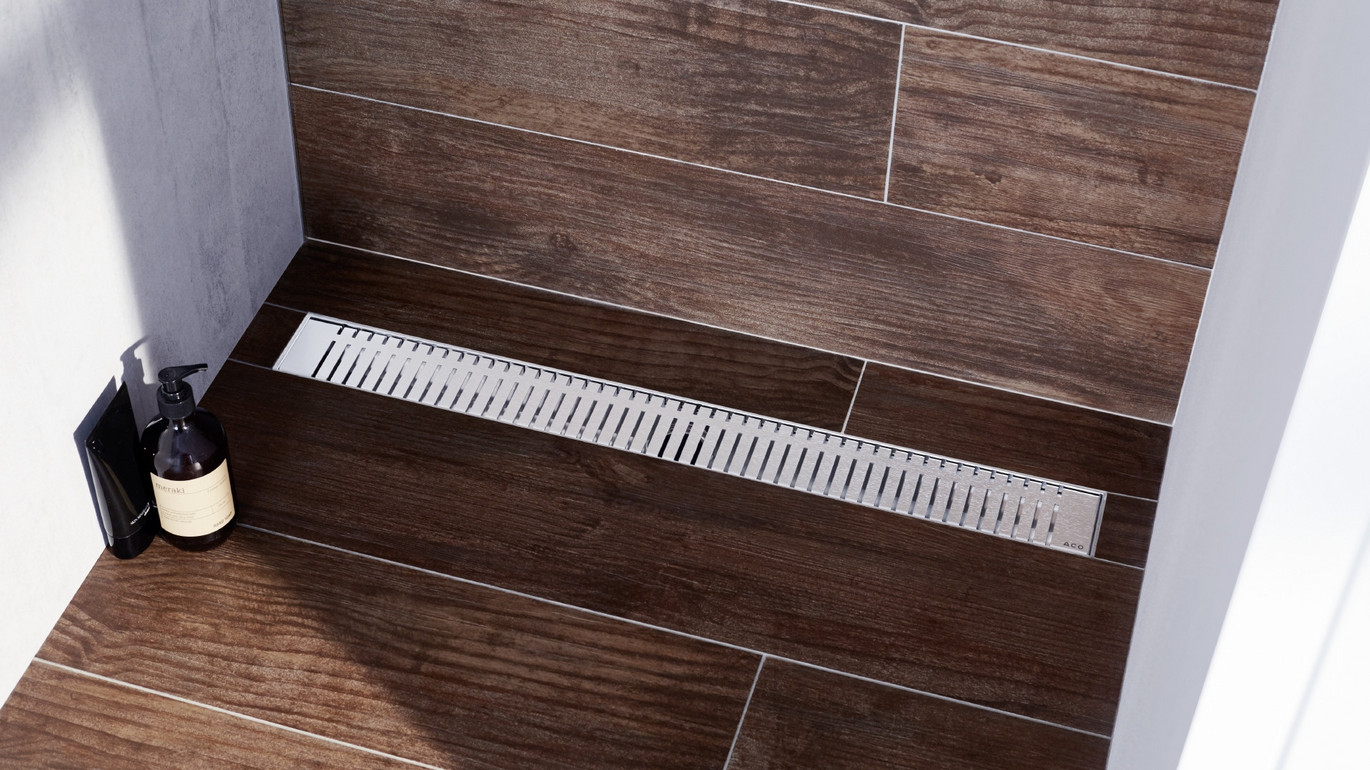 Dušas tekne Showerdrain M+ iestrādāta brūnās flīzes ar koka rakstu.
